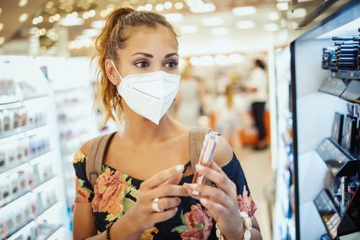 Shot of a young woman is wearing N95 protective mask while buying make-up in supermarket during Covid-19 pandemic.