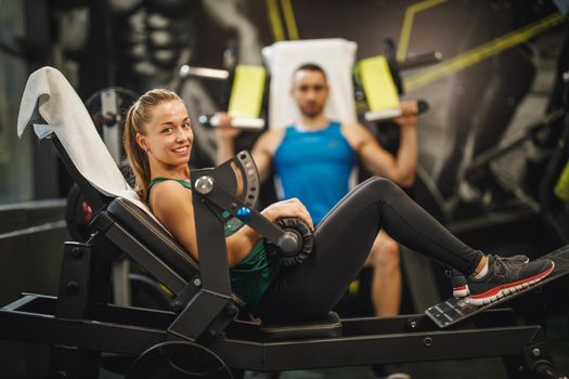 Shot of a muscular young woman in sportswear working out at the gym. She is doing glute bridge exercise for her gluteus on hip trust machine.