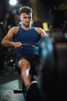 A young muscular man is pulling the row machine on crossfit training in the gym.