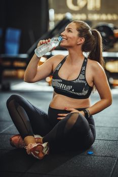 Shot of a pregnant woman drinking water and resting from her workout at the gym.