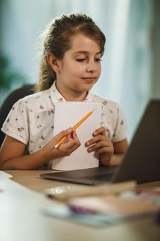 Shot of a diligent little girl using laptop to do a online lesson at home during COVID-19 pandemic.