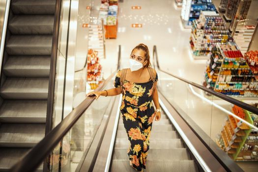 Shot of a young woman on an escalator in shopping mall is wearing N95 protective mask while buying during Covid-19 pandemic.