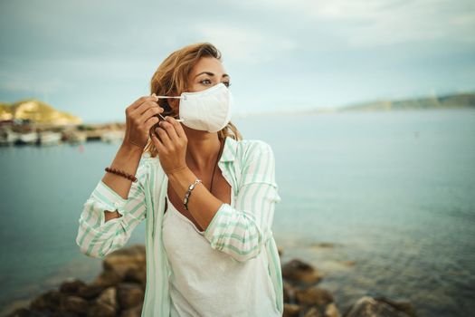 Shot of a happy young woman with protective N95 mask enjoying a vacation on the beach during the COVID-19.