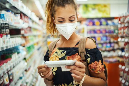 Shot of a young woman is wearing N95 protective mask while buying in supermarket during Covid-19 pandemic.