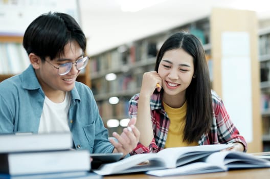 Young students campus helps friend catching up and learning. University students in cooperation with their assignment at library. Group of young people sitting at table reading books. Education and learning concept.