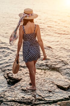 woman sea sunset. A woman in a dress, hat and with a straw bag is standing on the beach enjoying the sea. Happy summer holidays.