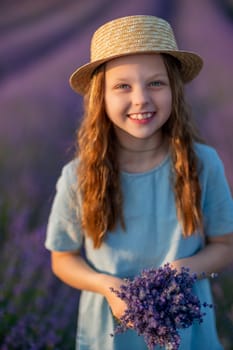 Lavender sunset girl. A laughing girl in a blue dress with flowing hair in a hat walks through a lilac field, holds a bouquet of lavender in her hands