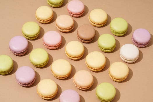 An overhead shot of a beige table surface featuring an array of colorful macarons in neat rows