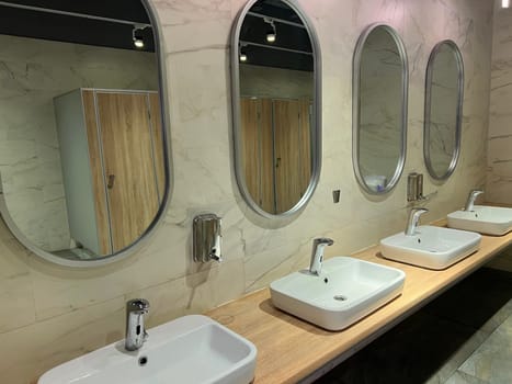 Modern restroom interior with stone gray tiles. Contemporary interior of public toilet. minimal interior with white tiles, round mirrors. Perspective of men's restroom. commercial bathroom.