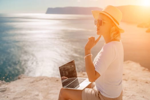 Freelance women sea working on the computer. Good looking middle aged woman typing on a laptop keyboard outdoors with a beautiful sea view. The concept of remote work