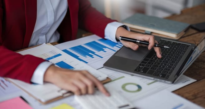 Close up Business woman using calculator and laptop for do math finance on wooden desk in office and business working background, tax, accounting, statistics and analytic research concept.