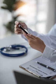 Hands of doctor in white coat using mobile phone, giving virtual online consultation, sending test results, chatting to patients, making video calls and appointments. Remote medical consulting.