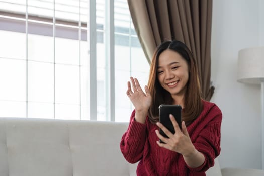 Young asian woman making video calling with smartphone using conferencing meeting online app at home. Happy teen girl waving to friend on phone screen.