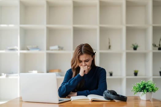 Tired asian woman bored with of laptop sad and frustrated about distance learning or online education sits at desk at home.