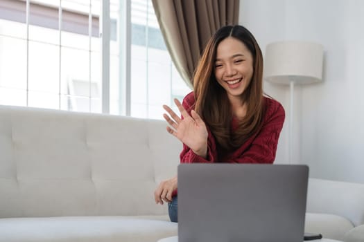 Young asian woman making video calling with laptop using conferencing meeting online app at home. Happy teen girl waving to friend on laptop screen.