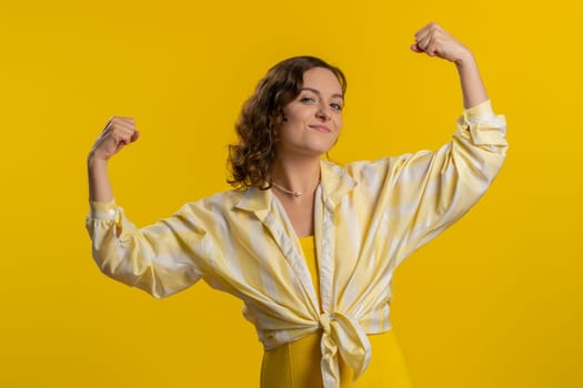 I am strong and independent. Young woman showing biceps and looking confident, feeling power strength to fight for rights, energy to gain success win. Girl isolated alone on yellow studio background