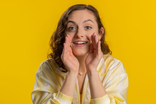 Keep my secrets, silence. Young woman whisper news rumors holding hands near mouth, share gossip, quiet. Girl telling interesting confidential story isolated on yellow studio background. Lifestyles