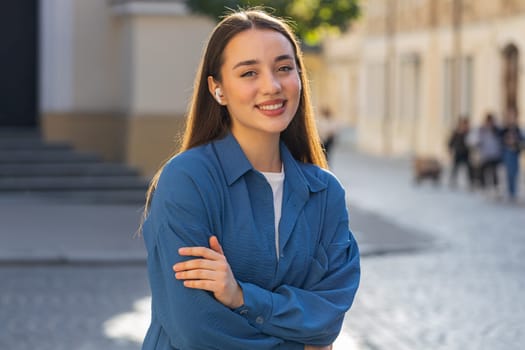 Happy relaxed overjoyed young pretty woman in wireless earphones choosing listening favorite energetic disco rock n roll music dancing looking at camera outdoors. Tourist girl walking in city street