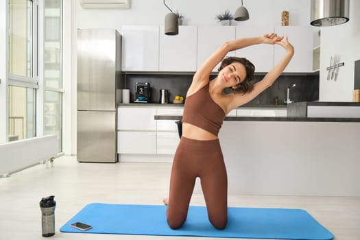 Woman stretching her body, doing fitness exercises. Fit and healthy girl workout at home in bright room. Copy space