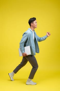Portrait of young man holding laptop, studio shot on yellow background