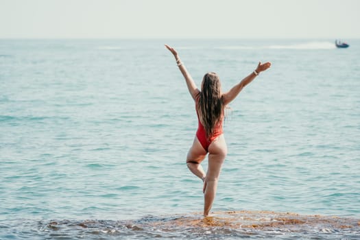 Woman sea yoga. Back view of free calm happy satisfied woman with long hair standing on top rock with yoga position against of sky by the sea. Healthy lifestyle outdoors in nature, fitness concept.