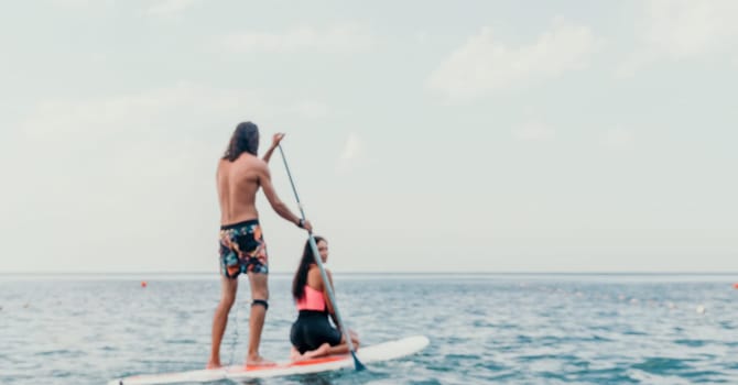 Sea woman and man on sup. Silhouette of happy young woman and man, surfing on SUP board, confident paddling through water surface. Idyllic sunset. Active lifestyle at sea or river