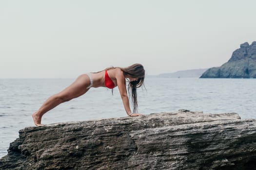 Woman meditating in yoga pose silhouette at the ocean, beach and rock mountains. Motivation and inspirational fit and exercising. Healthy lifestyle outdoors in nature, fitness concept.