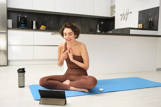 Woman, fitness instructor sitting on rubber mat, yoga couch talking to online group, recording class on tablet, remote training outside of gym, workout from home.