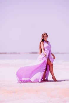 Woman pink salt lake. Against the backdrop of a pink salt lake, a woman in a long pink dress takes a leisurely stroll along the white, salty shore, capturing a wanderlust moment