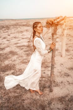 woman sea white dress. Model in boho style in a white long dress and silver jewelry on the beach. Her hair is braided, and there are many bracelets on her arms