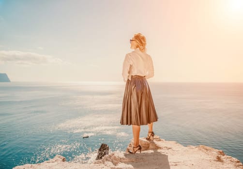 Business woman on nature in white shirt and black skirt. She works with an iPad in the open air with a beautiful view of the sea. The concept of remote work