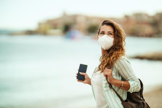 Shot of a happy young woman with protective N95 mask enjoying a vacation on the beach during the COVID-19.