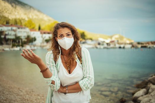 Shot of a concerned young woman with protective N95 mask at vacation on the beach during the COVID-19.