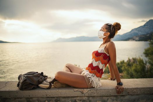 Shot of a happy young woman with protective mask spending time on seaside during exploring a Mediterranean at corona pandemic. 