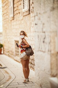 Shot of a happy young woman with protective mask spending time on vacation and exploring a Mediterranean city at corona pandemic. 