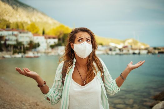 Pensive young woman with protective N95 mask feeling worried while spending time on the seaside during the COVID-19.