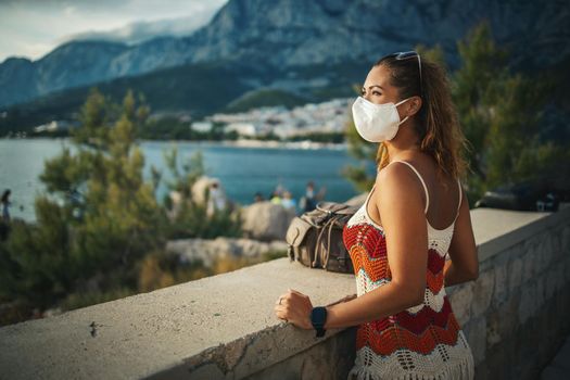 Shot of a happy young woman with protective mask spending time on seaside during exploring a Mediterranean at corona pandemic. 