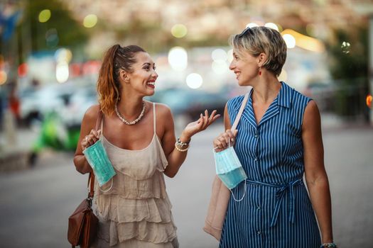 Shot of two attractive female friends who wear a surgical mask while exploring the wonderful city of Meditteranian.