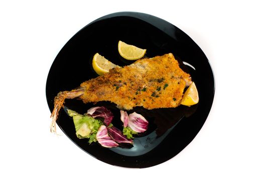 black plate with breaded monkfish on white background