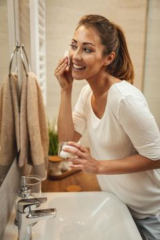 Shot of an attractive young woman wiping her face with a cotton pad in the bathroom at home.