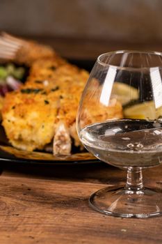 glass of white wine with fish plate behind on wooden 