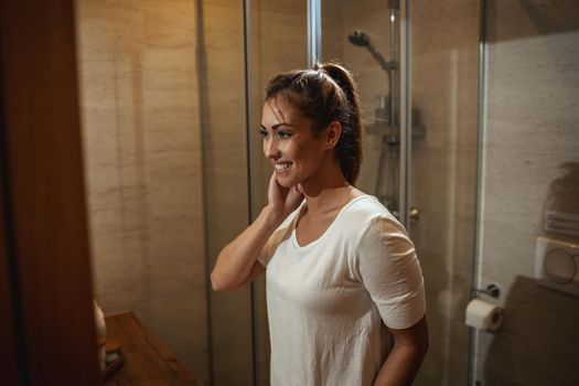 Attractive young woman admiring her face while standing in front of the bathroom mirror at home.