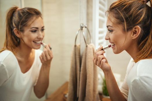 Shot of an attractive young woman applying lipstik on mirror in the bathroom at home.