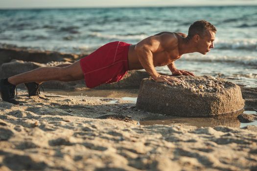 A handsome man ais doing push up exercise at the sea beach in summer sunny day.