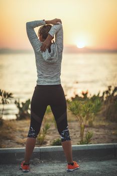 A beautiful young woman is doing stretching exercise by the sea in sunrise.