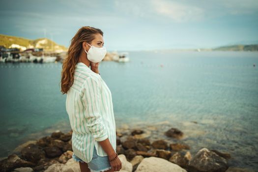 Shot of a young woman with protective N95 mask enjoying on the beach during the COVID-19.