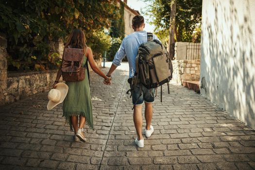 A beautiful young couple tourist arrived in a Mediterranean city, with a backpacks on their backs. They are enjoying in summer sunny day.