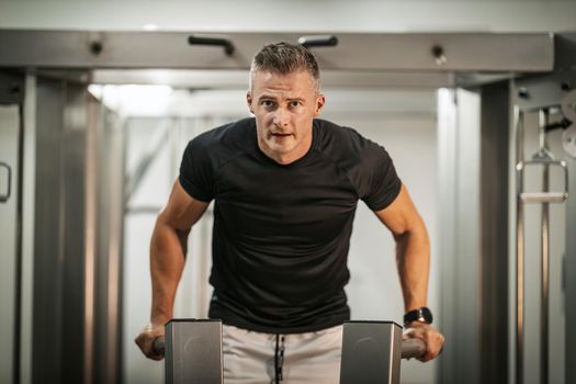 Muscular young man doing hard exercises on machine during a strength training workout at the gym.