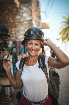 A beautiful young tourist arrived in a Mediterranean city with a backpack on her back and helmet on her head. She is enjoying in summer sunny day.
