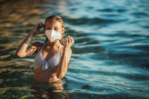 Shot of an happy teenager wearing surgical mask enjoying a vacation on the beach during the COVID-19. Looking at camera.